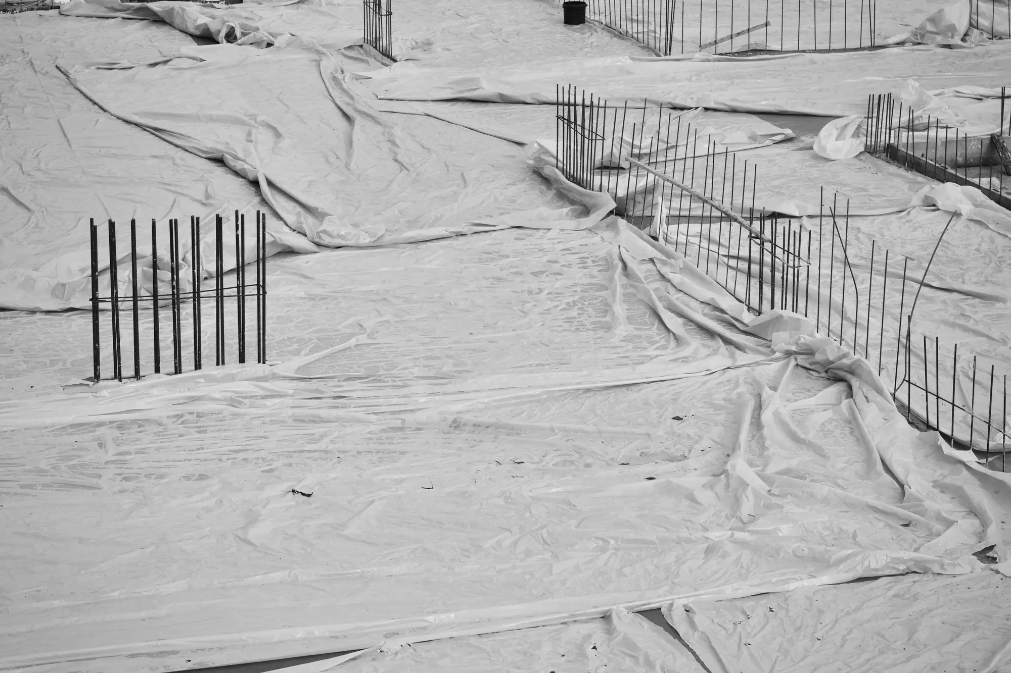 Foundations on a construction site covered over with plastic sheeting, rebar starter bars poking through