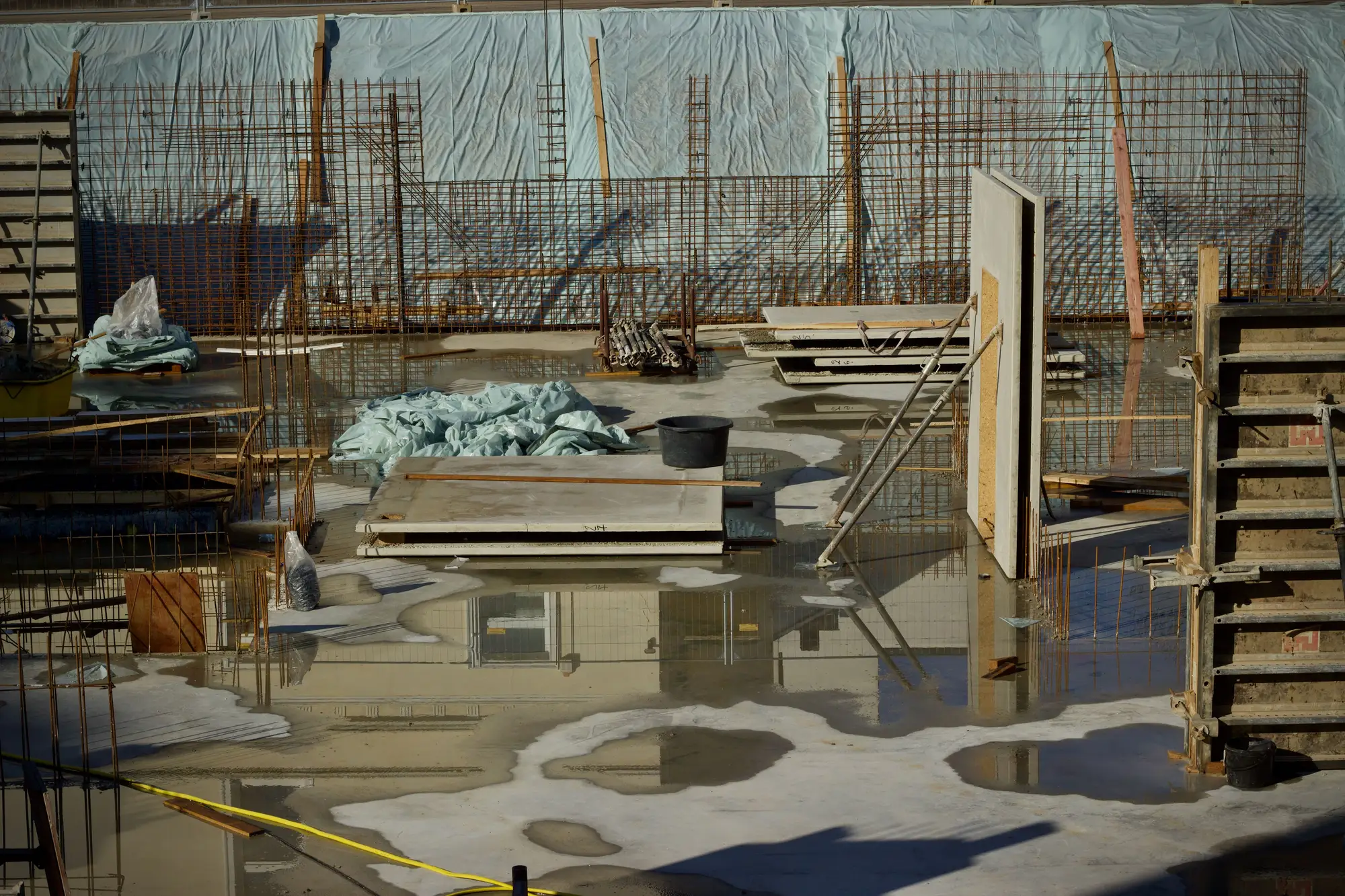 A formed slab on a construction site with rainwater standing between the rebar and stacked formwork
